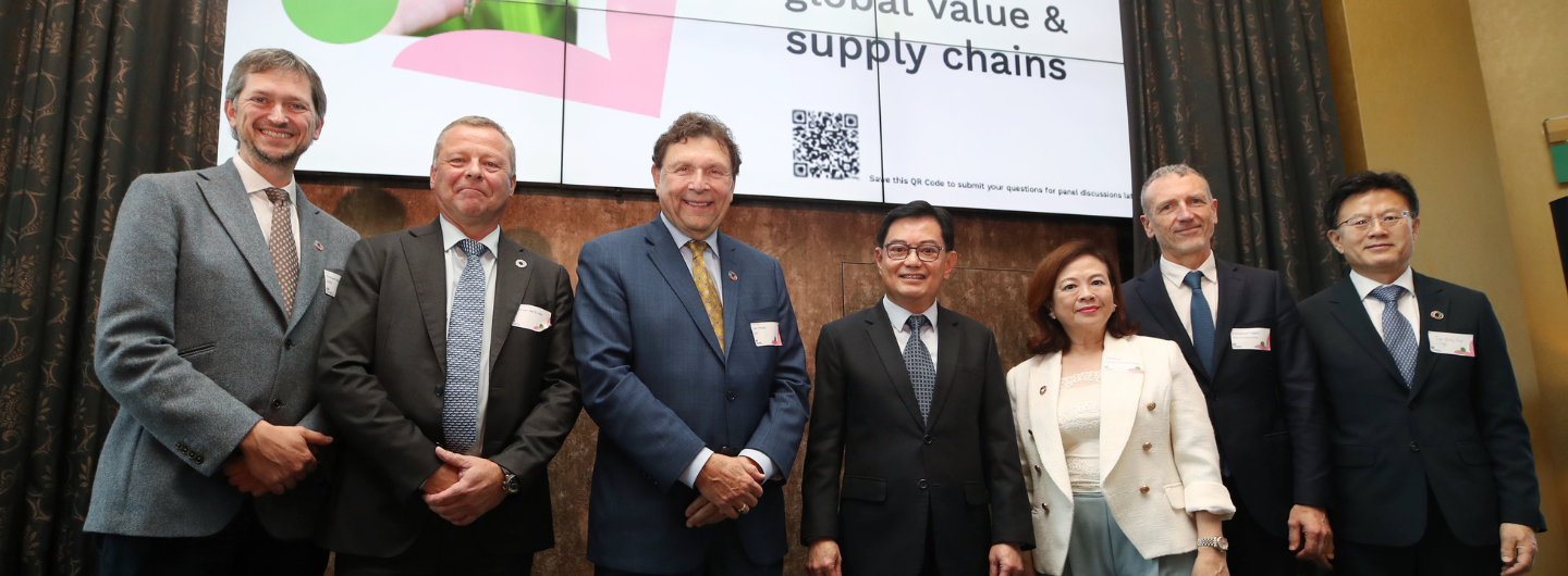 Group of eight formally dressed adults posing in front of a screen with a QR code.